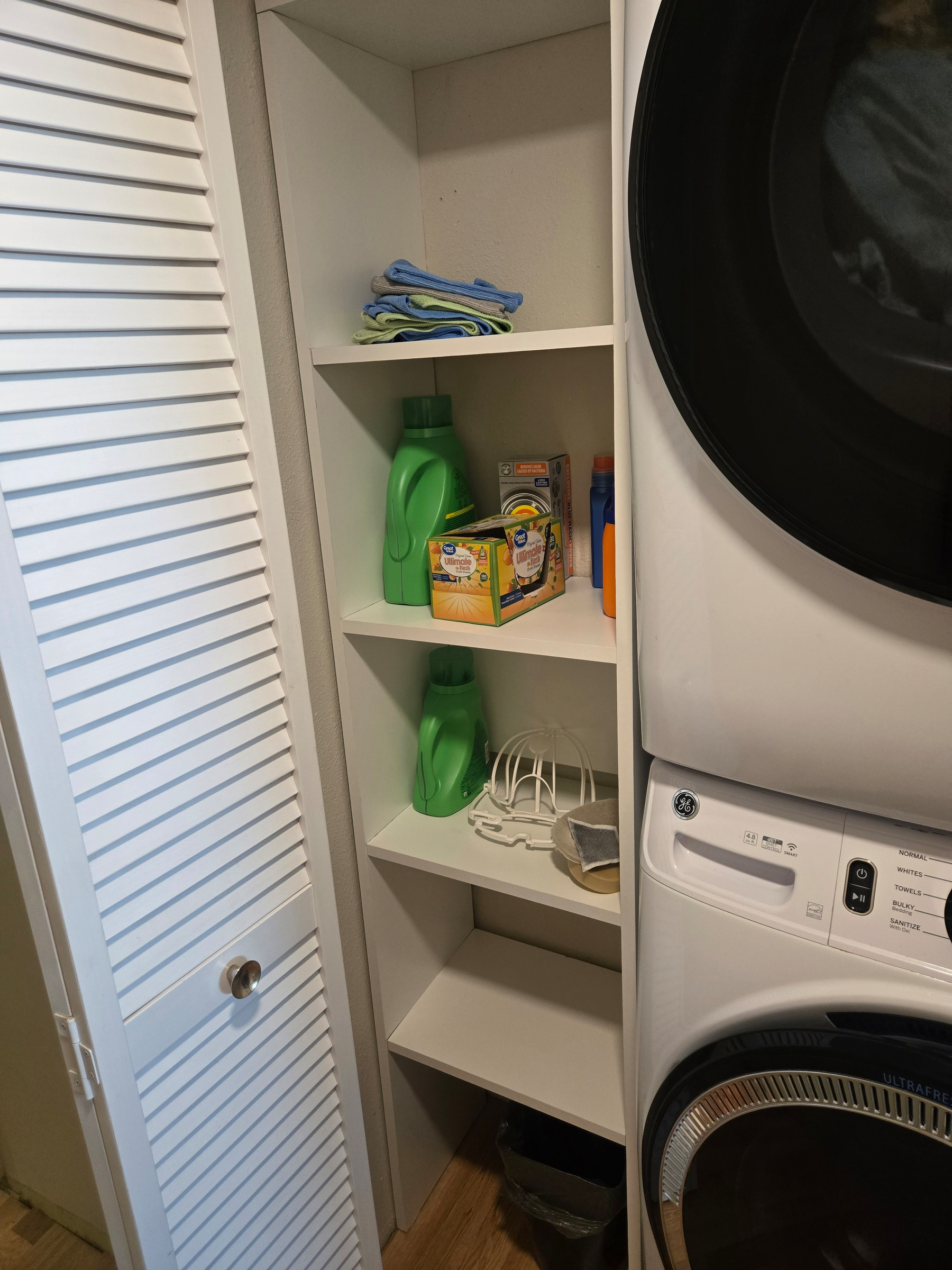 Photo of custom built shelves next to the laundry machines. There are four shelves in white melamine panel. Lots of storage!