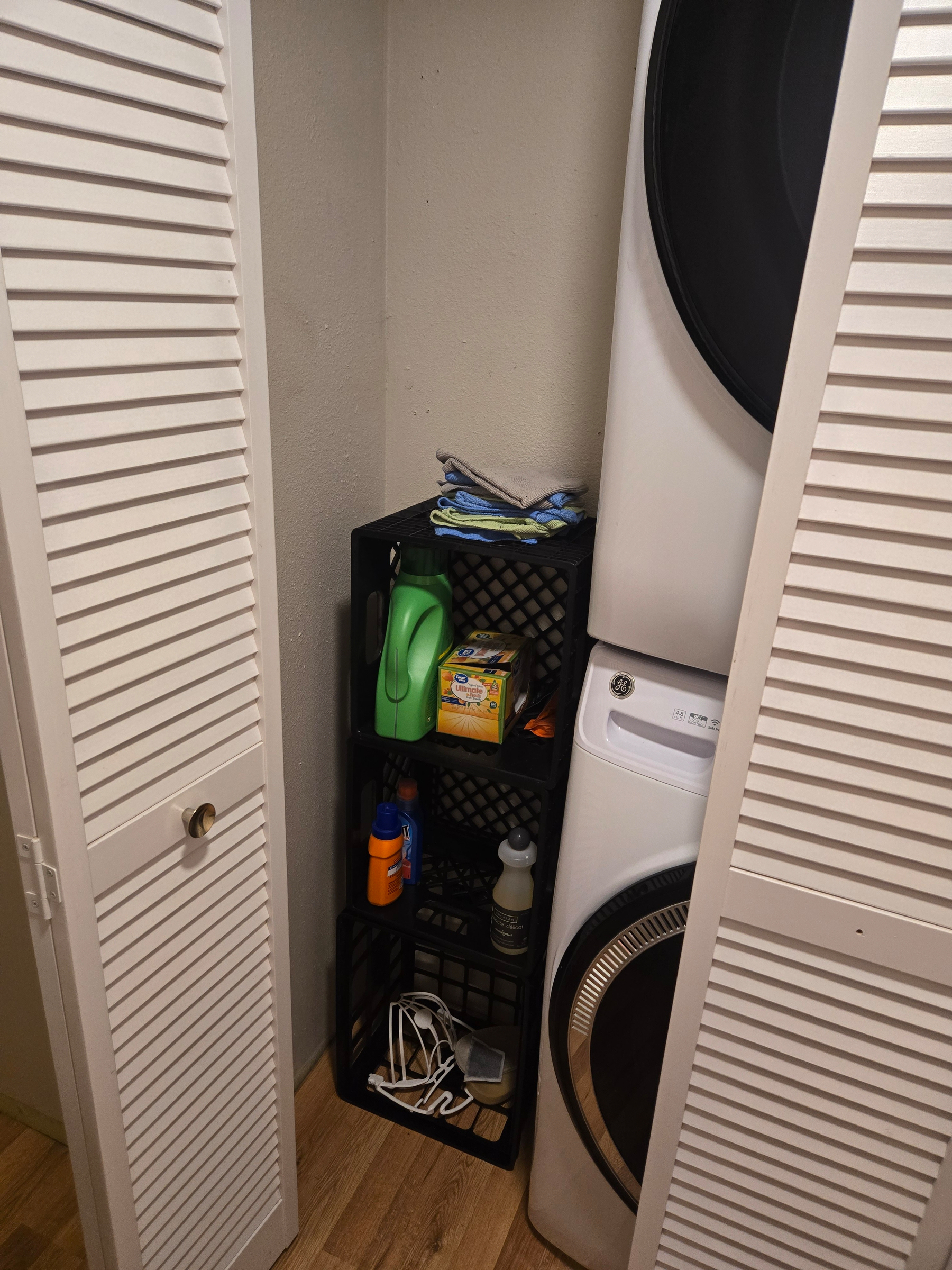 Before photo of a stack of black milk crates next to laundry machines in a closet with white foldable doors.
